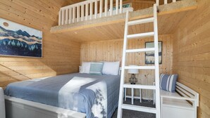 Ein Schlafzimmer einer Holzblockhütte mit Etagenbett, einer Leiter, einem Nachttisch und einem Bild an der Wand.