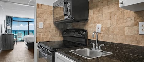 Uma cozinha moderna com fogão preto, pia de aço inoxidável e vista para uma varanda.