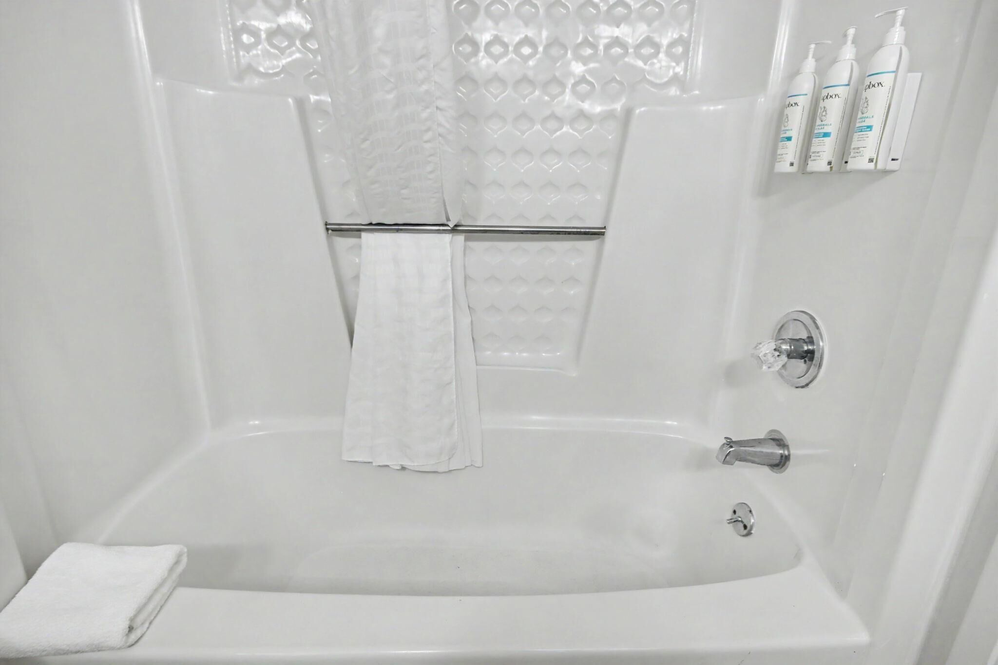 A white bathroom with a bathtub, a towel rack, and toiletries on the wall.