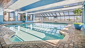 Una piscina interior con paredes de vidrio transparente, suelo de baldosas y techo azul.