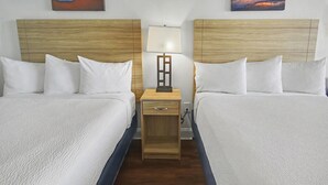 Una habitación de hotel con dos camas, una mesita de noche con una lámpara y obras de arte en las paredes.