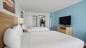 Ett hotellrum med två sängar, en tv, ett skrivbord och en dörr som leder till ett litet kök.