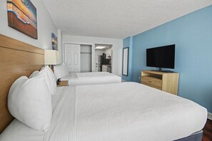 A hotel room with two beds, a television, a desk, and a door leading to a kitchenette. - Oceanfront Two Queen Room + Beach + Dog Friendly (Myrtle Beach)
