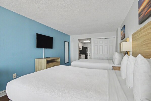 A hotel room with two beds, a TV, a desk, and a door leading to a bathroom.