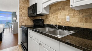 A modern kitchen with white cabinets, a black microwave, a stove, and a sink. - Oceanfront Two Queen Room + Beach + Dog Friendly (Myrtle Beach)
