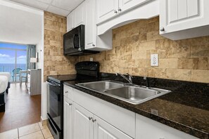A modern kitchen with white cabinets, a black microwave, a stove, and a sink.