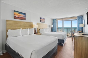 Habitació d'hotel amb dos llits, escriptori, cadira, televisió i un balcó amb vistes.