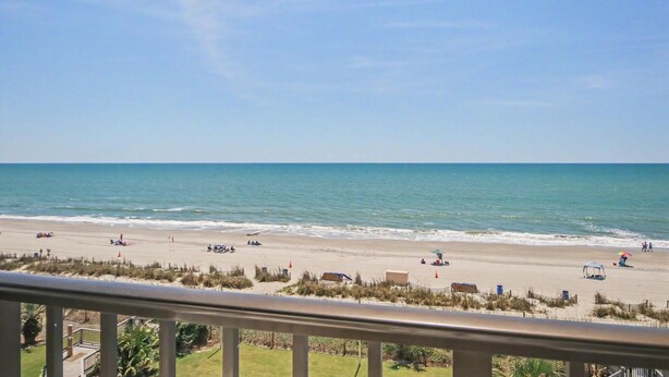 A beach view from a balcony with a railing, ocean, and beachgoers. - Oceanfront Two Queen Room + Beach + Dog Friendly (Myrtle Beach)