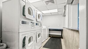 A laundry room with stacked washers and dryers, a black mat, and a tiled floor. - Oceanfront Two Queen Room + Beach + Dog Friendly (Myrtle Beach)