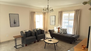 Un salon comprenant un canapé, deux fauteuils, une table basse, un meuble pour la télévision et un lustre.