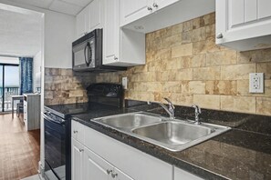 A modern kitchen with a double sink, stainless steel appliances, and a stone backsplash. - Oceanfront Two Queen Room + Beach + Dog Friendly (Myrtle Beach)