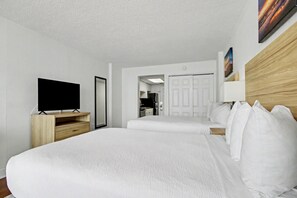 A hotel room with a large bed, a TV on a wooden stand, a wardrobe, and a door leading to a bathroom. - Oceanfront Two Queen Room + Beach + Dog Friendly (Myrtle Beach)