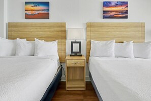 A hotel room with two beds, a nightstand with a lamp, and two paintings on the wall. - Oceanfront Two Queen Room + Beach + Dog Friendly (Myrtle Beach)