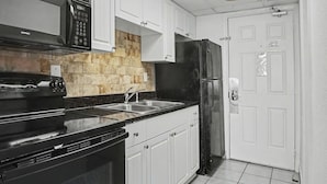 Una cocina con armarios blancos, estufa negra, refrigerador negro y salpicadero de piedra.