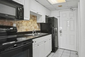 A kitchen with white cabinets, a black stove, a black refrigerator, and a stone backsplash. - Oceanfront Two Queen Room + Beach + Dog Friendly (Myrtle Beach)