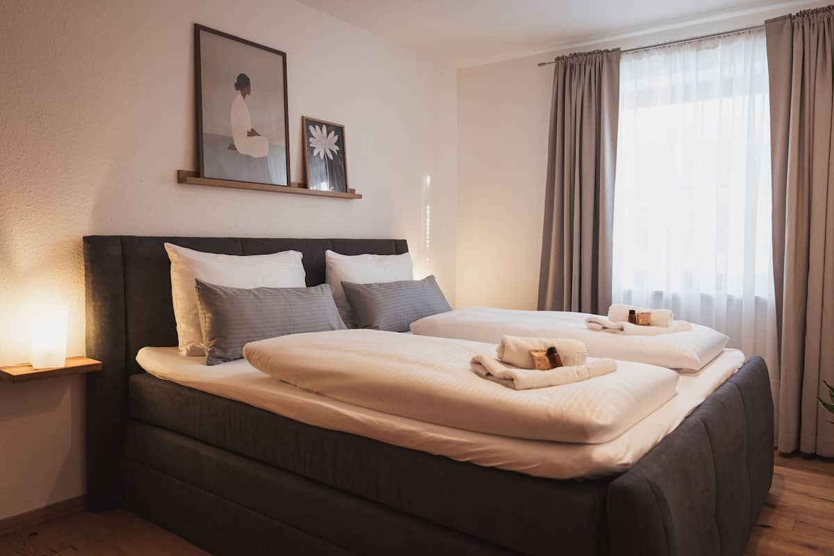 A double bed with a dark headboard, two bedside tables with lamps, a framed picture above the bed, and a window with curtains.