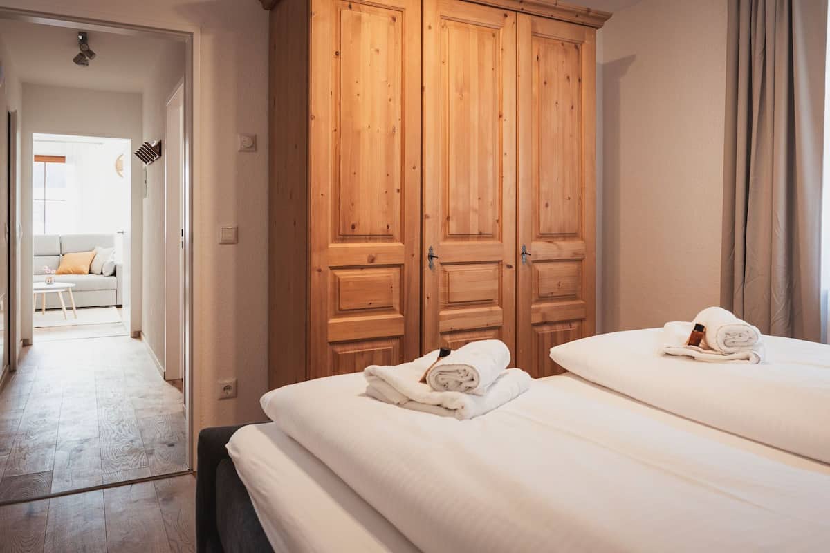 A hotel room with two beds, wooden wardrobes, a sofa in the adjacent room, and a window with curtains.
