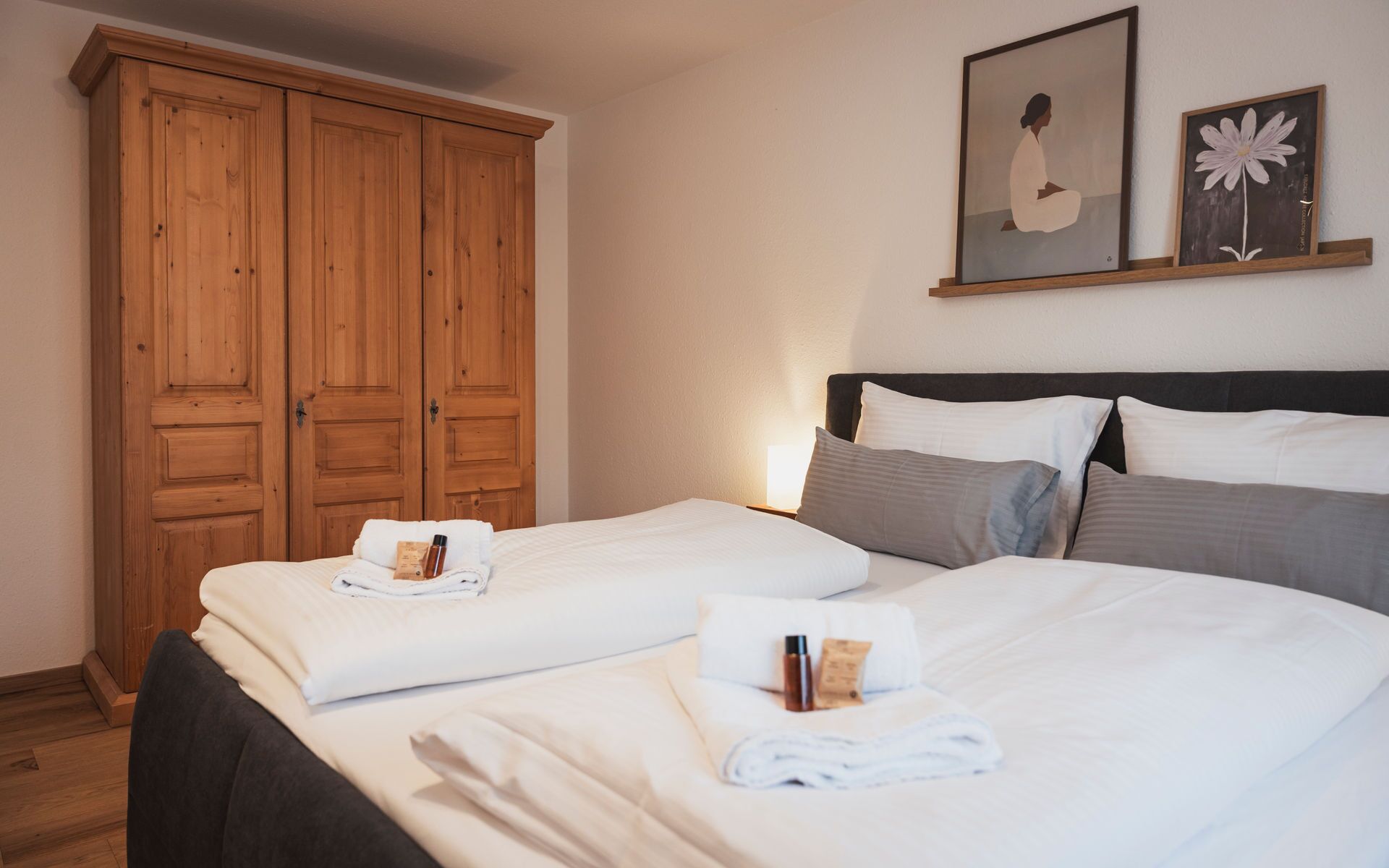 A hotel room with two beds, wooden wardrobe, and artwork on the wall.