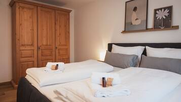 A hotel room with two beds, wooden wardrobe, and artwork on the wall.