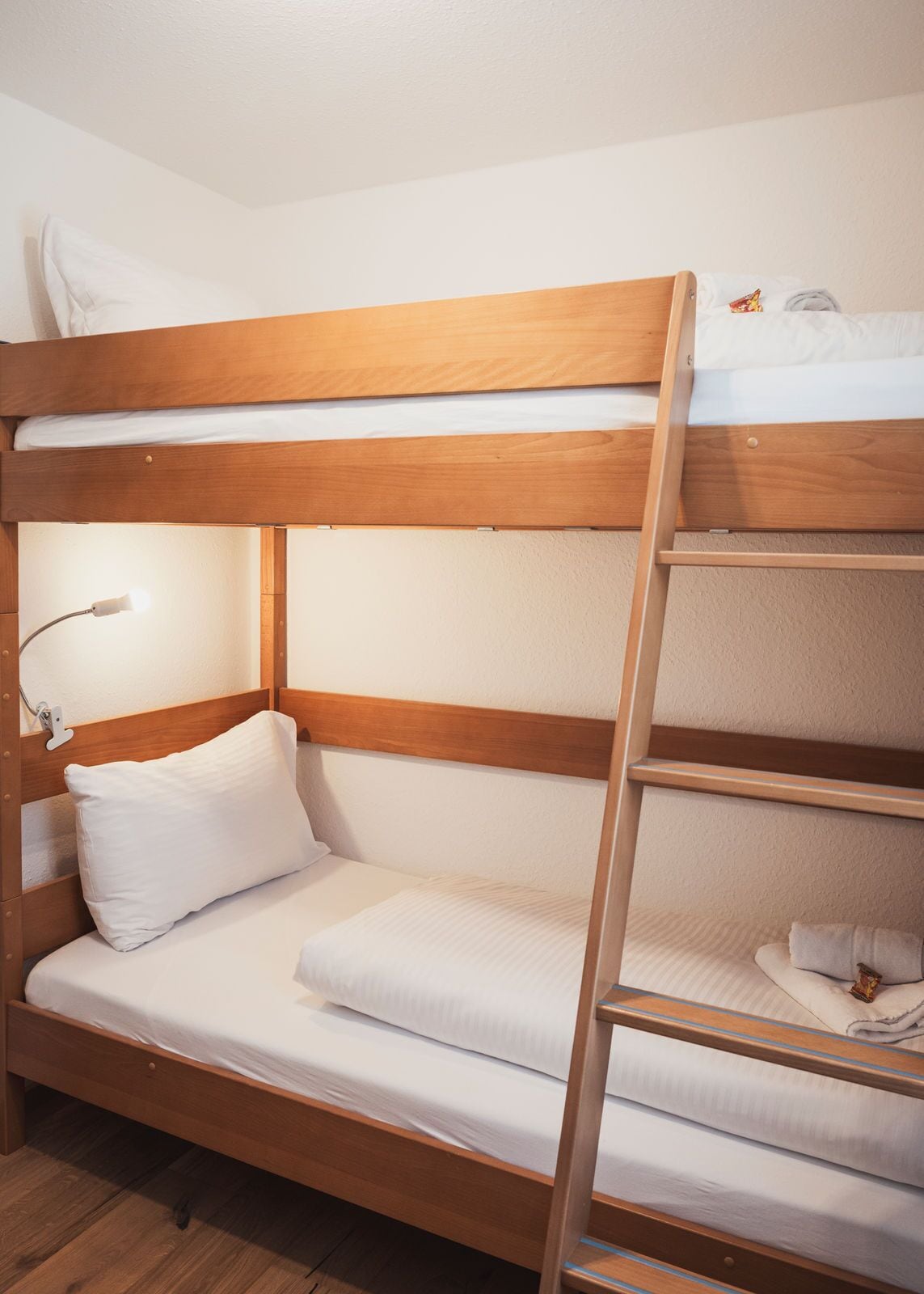 Un letto a castello con struttura in legno, una lampada da comodino e un piccolo ripiano con un asciugamano.