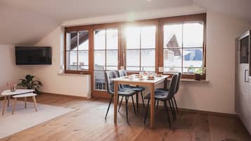 A dining area with a table set for breakfast, large windows, a flat-screen TV, and a potted plant.