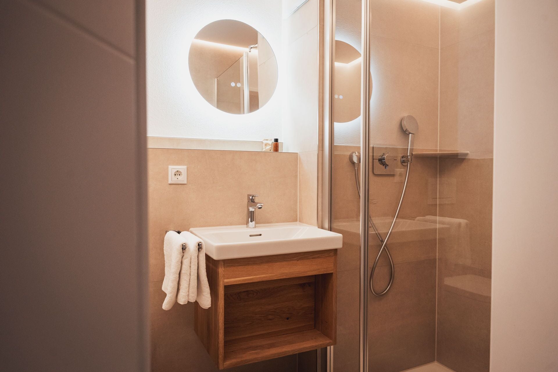 Un baño moderno con ducha de vidrio, tocador de madera con lavamanos y espejo sobre el tocador.