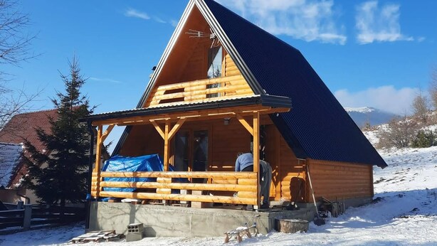 A wooden cabin with a sloped roof, a porch, and a clear blue sky.