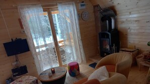 A cozy cabin interior with a fireplace, a television mounted on the wall, and a large window with curtains.