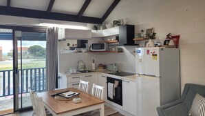 A compact kitchen with a dining table, chairs, a microwave, a refrigerator, and a small oven. - Cosy Reef View Apartment overlooking Sunset Coast, Fishing, Sand Dunes, Beaches. (Lancelin)