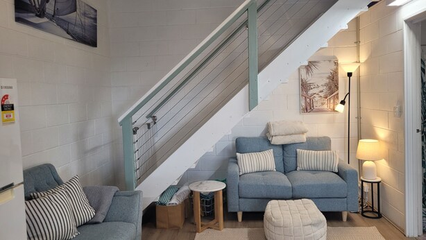 A living room with a staircase, a sofa, a small round table, and a lamp. - Cosy Reef View Apartment overlooking Sunset Coast, Fishing, Sand Dunes, Beaches. (Lancelin)