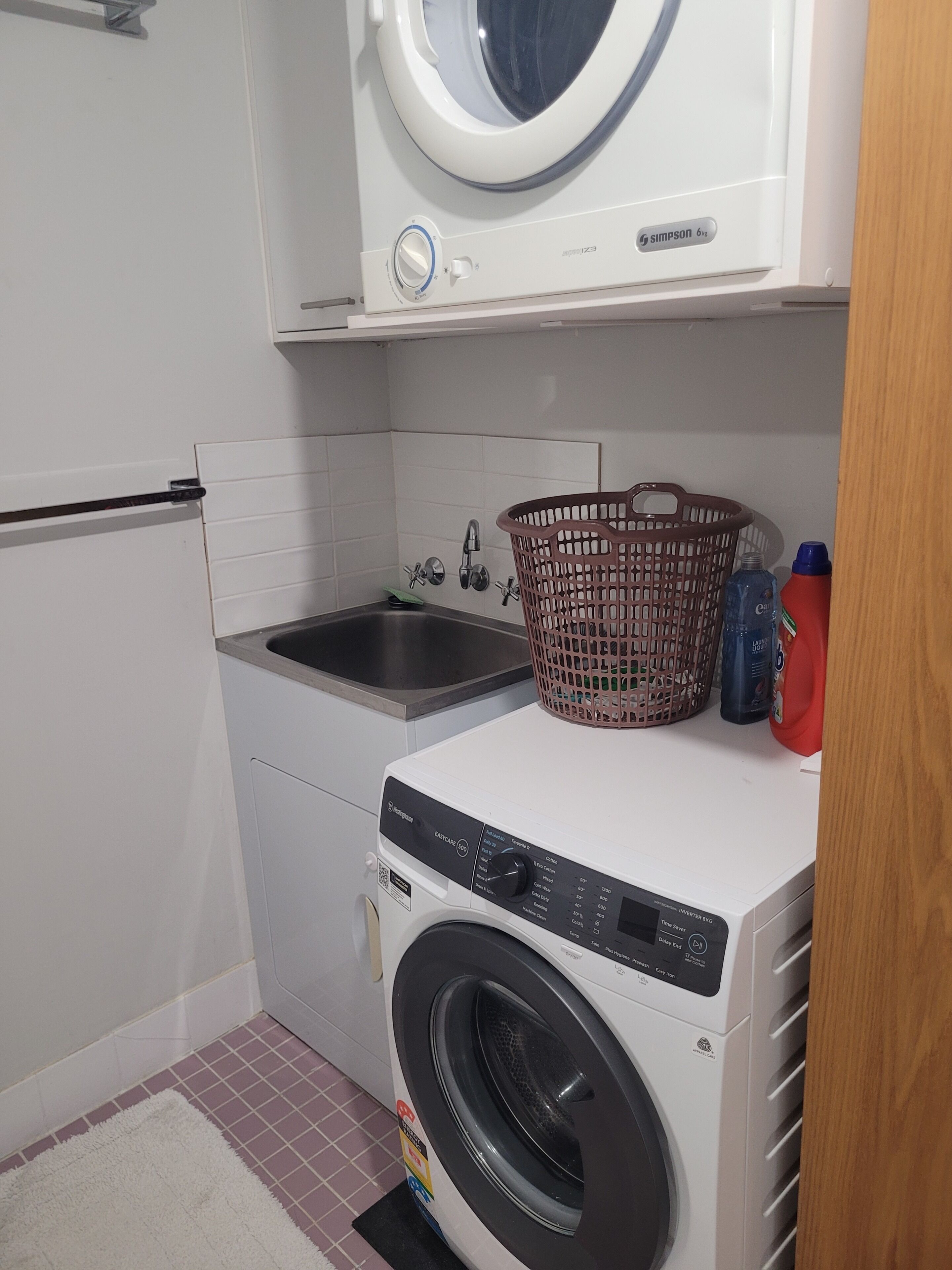 A compact laundry area with a washing machine, a sink, and a basket.