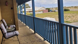 A covered outdoor area with a blue railing, a concrete floor, and a few chairs. - Cosy Reef View Apartment overlooking Sunset Coast, Fishing, Sand Dunes, Beaches. (Lancelin)