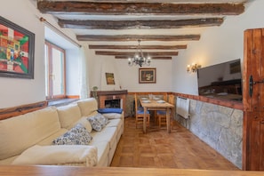 Um quarto acolhedor com teto de madeira, um sofá com almofadas, uma mesa de jantar posta para quatro e uma parede de pedra.