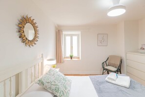 A bedroom with a bed, a chair, a dresser, a mirror, a window, and a ceiling light.
