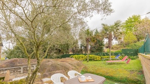 Un patio con mesa, sillas y un pequeño jardín con diversas plantas y una roca.