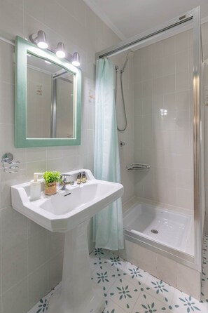 Une salle de bain avec un lavabo blanc, un miroir avec éclairage intégré, une douche avec une porte en verre et des carreaux de sol à motifs.