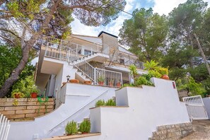 A multi-story building with a staircase leading to a balcony, surrounded by trees and potted plants. - Holiday Villa Beauty Can Picafort (Can Picafort)