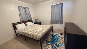 Un dormitorio con cama, mesita de noche, lámpara, cómoda y alfombra con diseño de cangrejo.