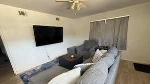 A living room with a grey sofa, a coffee table, a flat-screen TV, and a ceiling fan. - 3-bedroom house in enchanting Fort Walton Beach with AC (Fort Walton Beach)