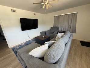 A living room with a grey sofa, a coffee table, a flat-screen TV, and a ceiling fan. - 3-bedroom house in enchanting Fort Walton Beach with AC (Fort Walton Beach)