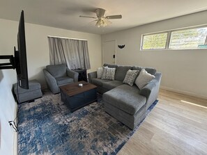 A living room with a grey sofa, a coffee table, a TV, and a ceiling fan. - 3-bedroom house in enchanting Fort Walton Beach with AC (Fort Walton Beach)