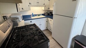 A compact kitchen with white cabinets, a gas stove, a white refrigerator, and a blue countertop. - 3-bedroom house in enchanting Fort Walton Beach with AC (Fort Walton Beach)
