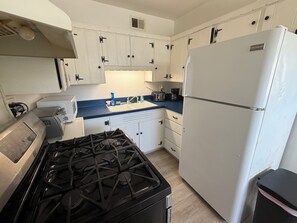 A compact kitchen with white cabinets, a gas stove, a white refrigerator, and a blue countertop. - 3-bedroom house in enchanting Fort Walton Beach with AC (Fort Walton Beach)
