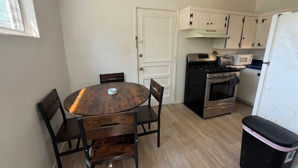 A compact kitchen with a round wooden table, two chairs, a stove, a microwave, and a refrigerator. - 3-bedroom house in enchanting Fort Walton Beach with AC (Fort Walton Beach)