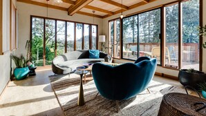 Una habitación amplia con ventanas grandes, un sofá, una silla azul y una mesa de centro.