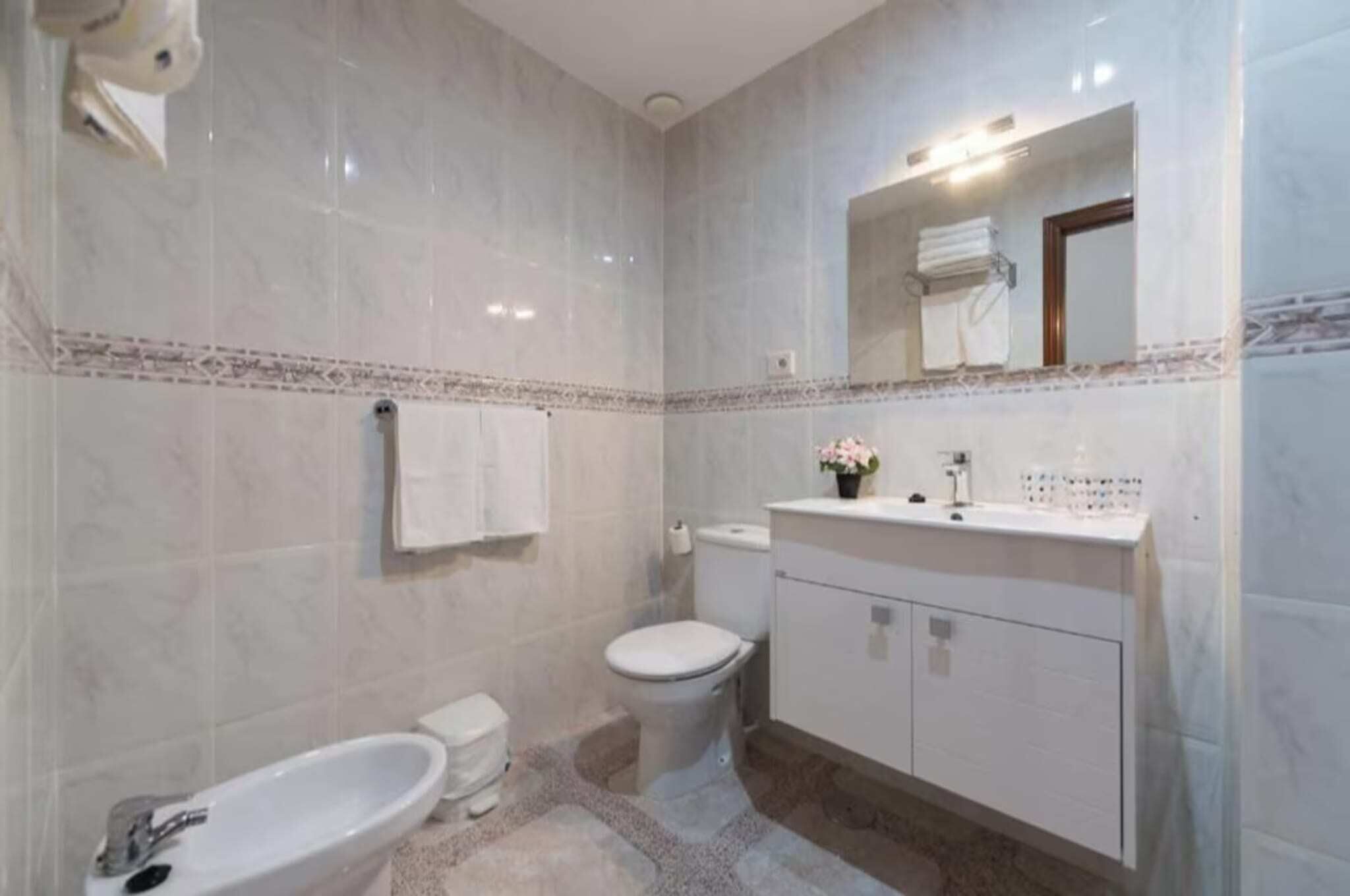 A bathroom with a toilet, bidet, sink, and mirror.