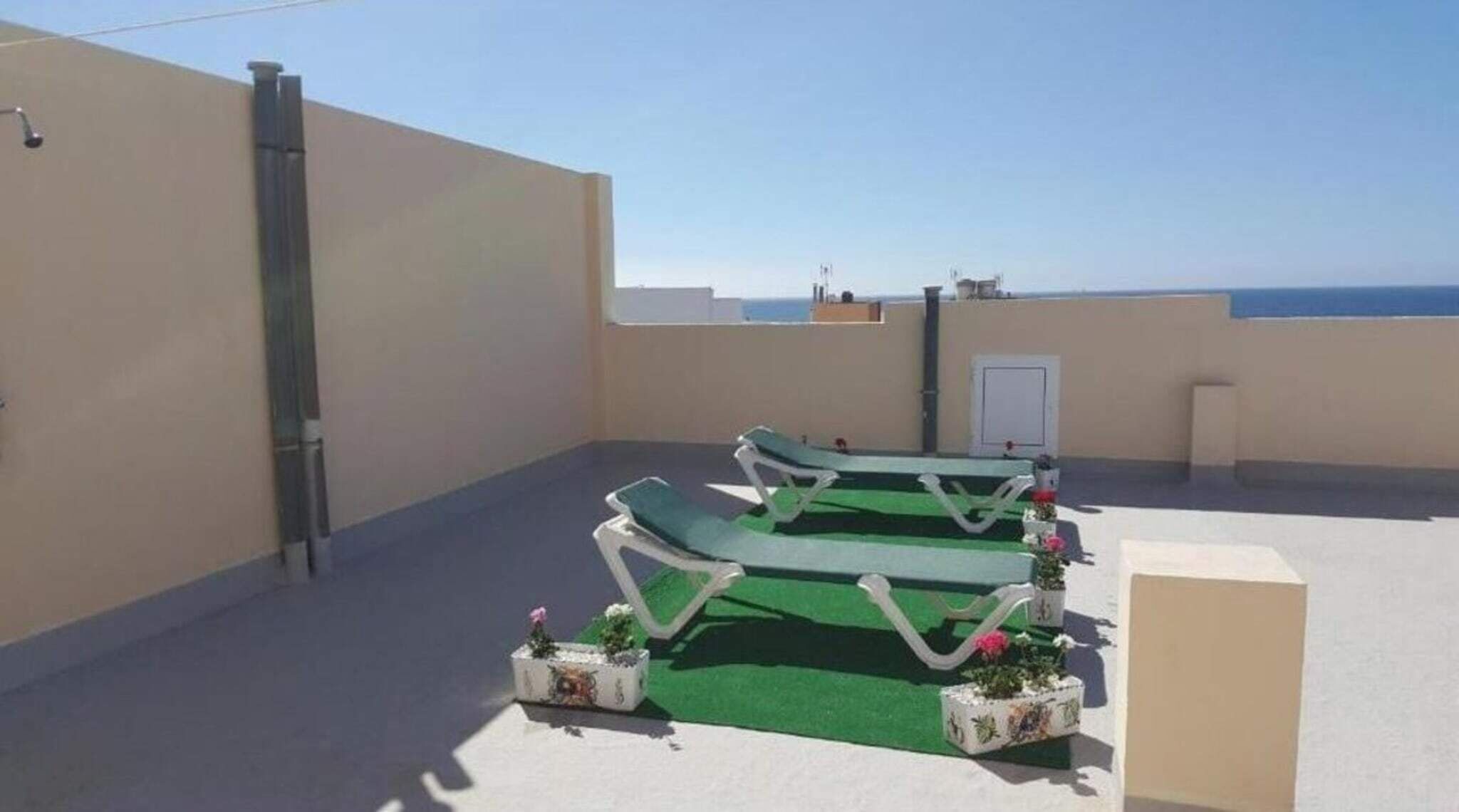 A rooftop terrace with two lounge chairs, a small table, and potted plants.