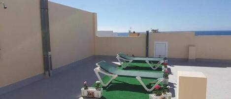 A rooftop terrace with two lounge chairs, a small table, and potted plants.
