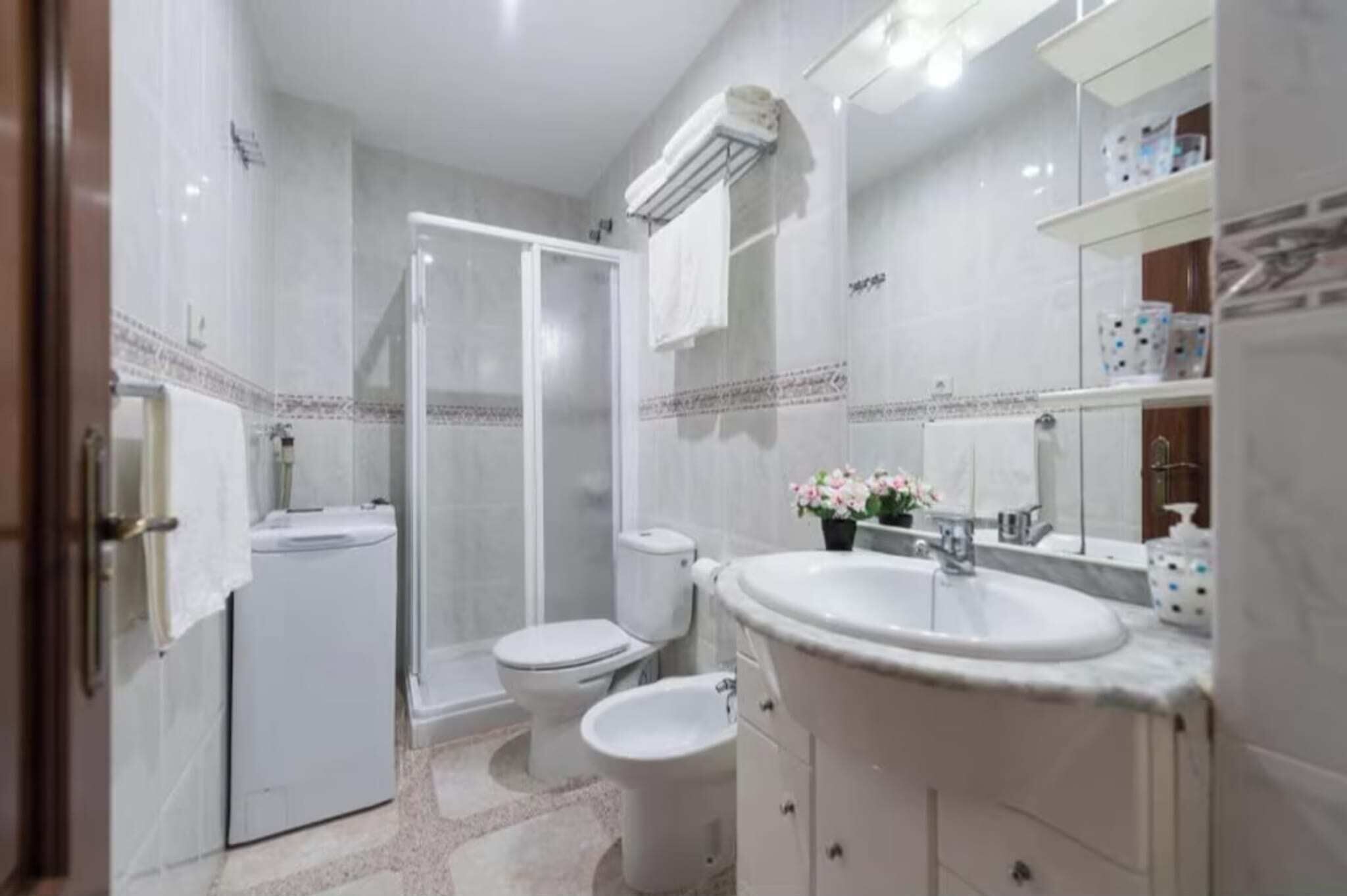 A bathroom with a shower, toilet, bidet, and sink.