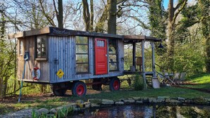 A small wooden house with a red door, windows, and a porch area.